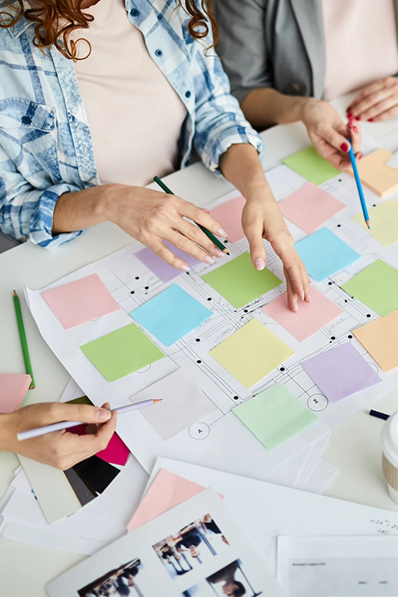 Overhead view of a team creating a project roadmap on paper grid with colorful square sticky notes, symbolizing agile planning and collaboration.
